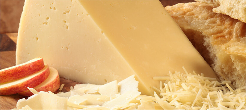 Asiago cheese portion on a wood cutting board with sliced and finely grated varieties.